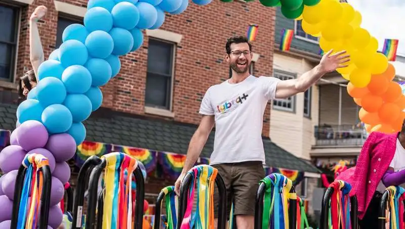 Szenenbild: weißer Mann winkt von Pride Parade Wagen