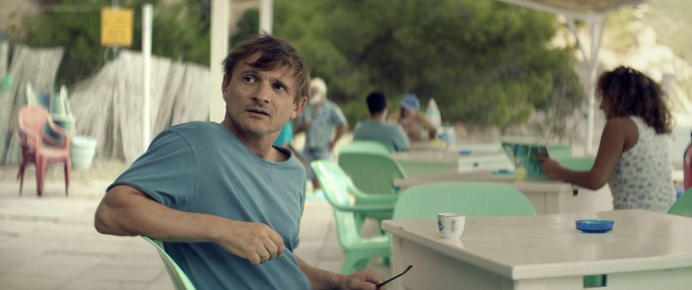 sommerliches Wetter, ein Mann im T-Shirt sitzt unter freiem Himmel an einem Tisch in einem Ferienressort