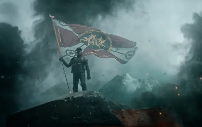 ein junger Mann in Rüstung steht auf der Spitze eines Felsens, er hält eine riesige Fahne in der Hand, auf der verschiedene Symbole abgebildet sind, im Hintergrund sind schneebedeckte Berge zu sehen, dunkler Rauch steigt um den Mann herum auf
