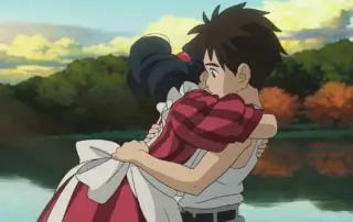 im Vordergrund umarmt ein schwarzhaariges Mädchen im roten Rüschenkleid einen Jungen mit weißen Hemd und grauer Hose, im Hintergrund sind ein See und angrenzende Bäume zu sehen