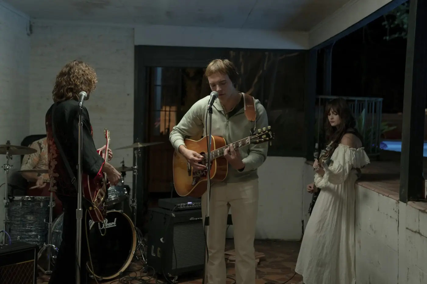 Eine Band spielt in einem häuslichen Vorbau, es ist Nacht. Im Vordergrund stehen zwei Männer, die auf Gitarren spielen, links von ihnen steht eine junge Frau im weißen Kleid und mit Gitarre. Im Hintergrund sitzt ein Mann am Schlagzeug.