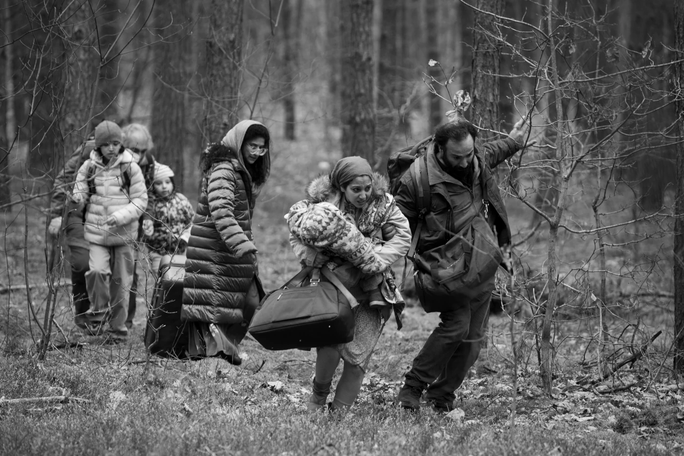 eine kleine Gruppe von Menschen mit Gepäck und in dicken Jacken stapft durch einen Wald