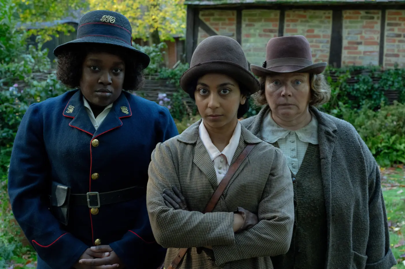 drei Frauen, gekleidet in Mäntel und Uniformen aus den 1920ern sowie jeweils einen Hut tragend, schauen erwartungsvoll in die Kamera