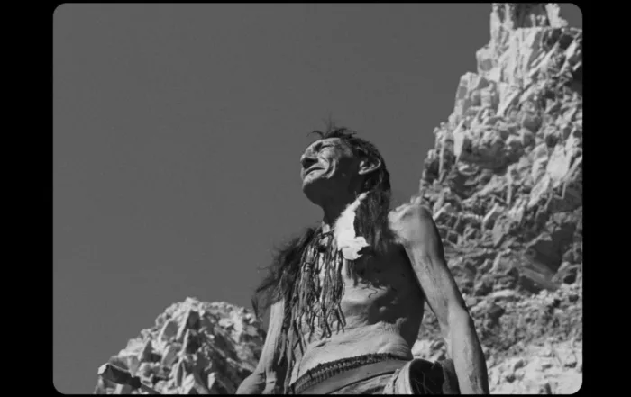 ein Bild in Schwarzweiß, ein Mann steht oberkörperfrei auf einem Felsen und schaut in die Ferne