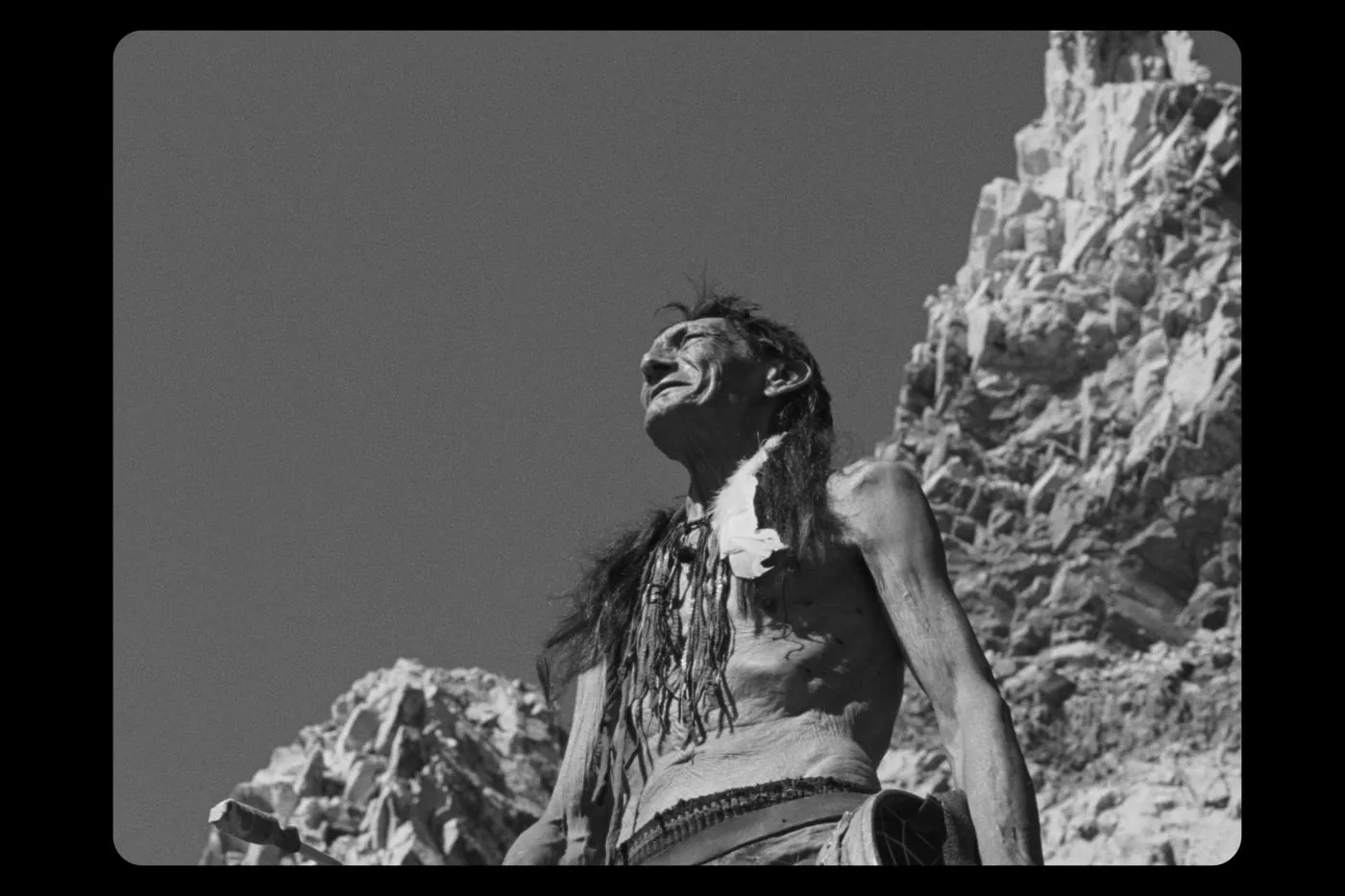ein Bild in Schwarzweiß, ein Mann steht oberkörperfrei auf einem Felsen und schaut in die Ferne