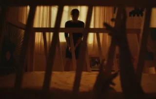 eine Frau steht vor einem Kinderbett, an den Gitterstäben des Bettes klettern kleine Hände empor