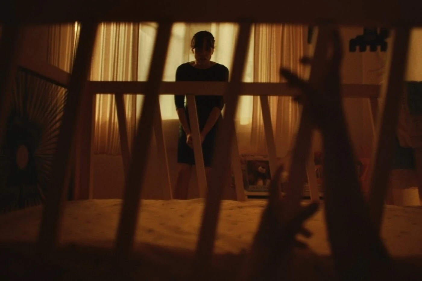 eine Frau steht vor einem Kinderbett, an den Gitterstäben des Bettes klettern kleine Hände empor