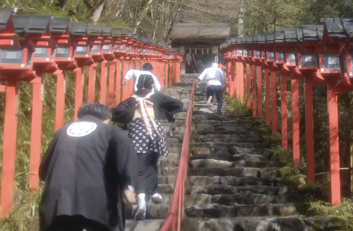 vier Hotelangestellte laufen eine Steintreppe hinauf, links und rechts stehen rote Laternenpfähle, am Ende der Treppe steht ein kleiner Tempel
