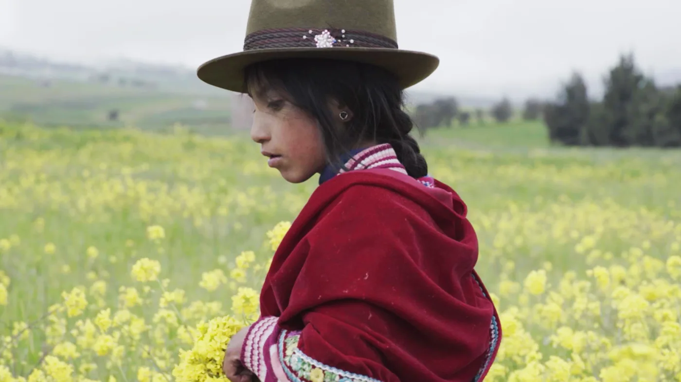 halbnahe Aufnahme eines Mädchens mit einem braunen Hut, das über eine gelbblühende Blumenwiese streift