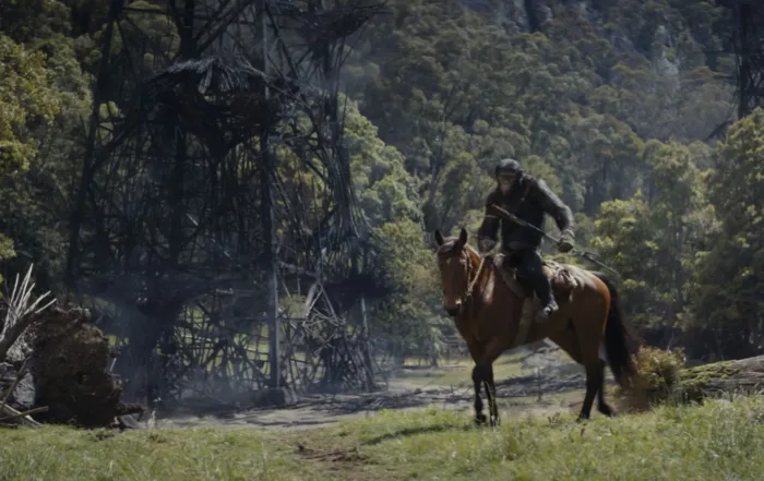 eine bewaldete Landschaft von Trümmern übersät, rechts im Bild reitet ein bewaffneter Schimpanse auf einem braunen Pferd