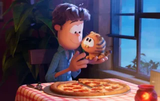 ein Abend im Restaurant, ein Mann sitzt allein an einem Tisch am Fenster, vor ihm eine große Salami-Pizza, auf der linken Hand sitzt ein kleines orange-schwarz gestreiftes Kätzchen