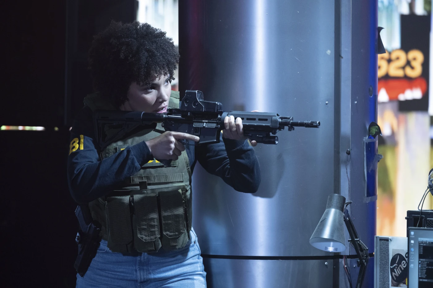 eine bewaffnete Frau mit Warnweste und Maschinengewehr richtet ihre Waffe auf ein Ziel außerhalb des Bildes