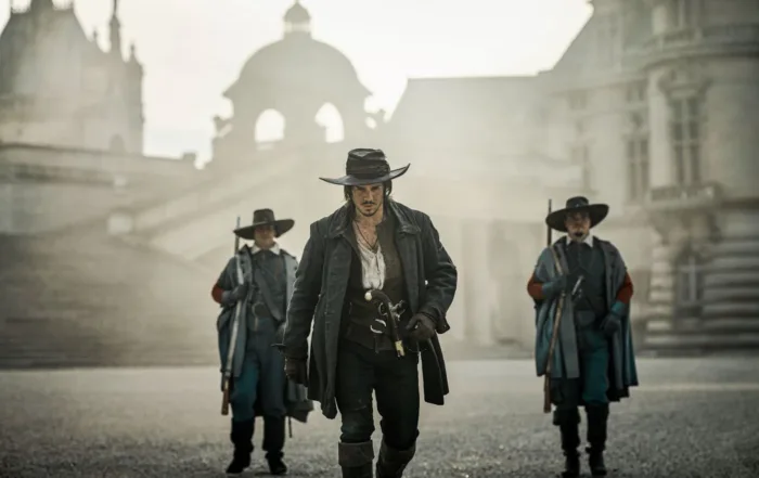 ein leergefegter Platz, die drei Musketiere im Mantel und mit Degen gehen auf die Kamera zu