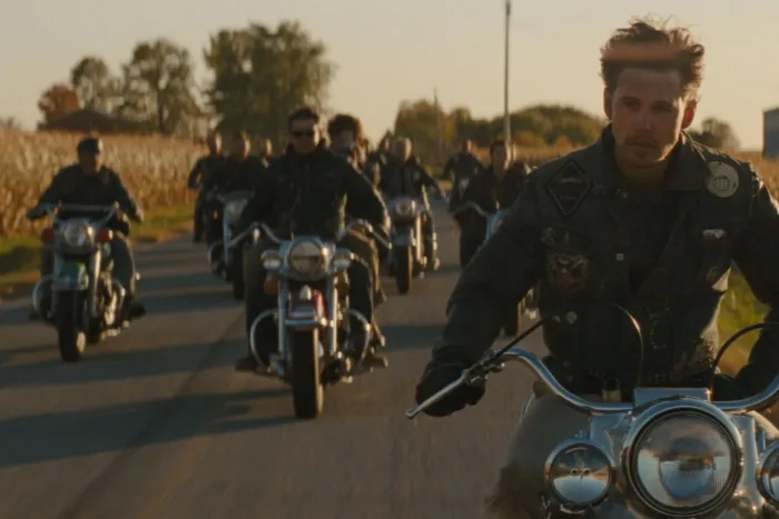 eine sonnenbeschienene Landstraße, eine Biker-Kolonne fährt auf die Kamera zu, ihnen voran ein Mann ohne Helm in schwarzer Lederjacke