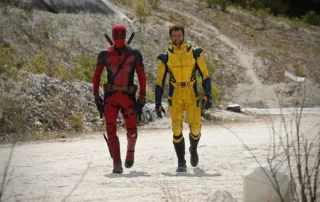 eine kahle, hügelige Wüstenlandschaft, mittig im Bild marschieren Deadpool im rot-schwarzen und Wolverine im gelb-blauen Anzug auf die Kamera zu