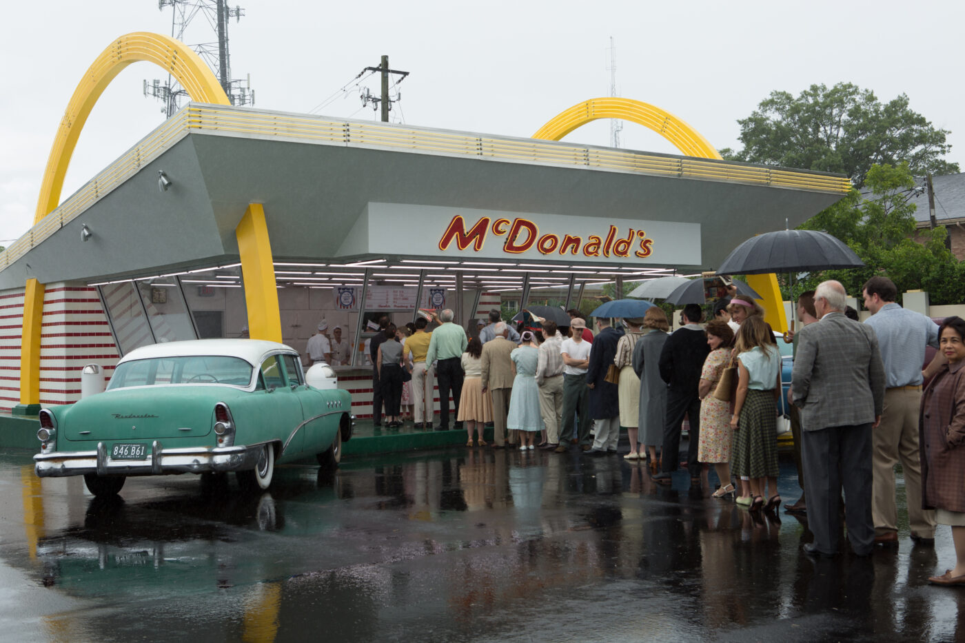 1950er Jahre, vor einer McDonalds Filiale reiht sich eine Menschenschlange bei Regenwetter