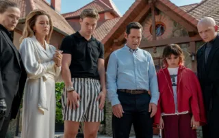 sechs Menschen stehen vor einem Haus und schauen vor sich auf den Boden