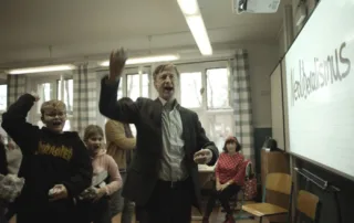 Jan Henrik Stahlberg als Mux vor einer Schulklasse mit geballter Faust skandierend