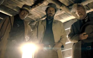 Henry Tibbs (Tyler Gaisford), Wood Helm (Josh Hopkins) und Drum (Jake Busey) als Cowboys in einer Scheune, sie schauen von oben auf die Kamera herab