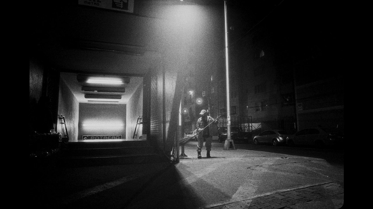 eine Straße bei Nacht, eine Frau im Putzanzug säubert den Gehweg