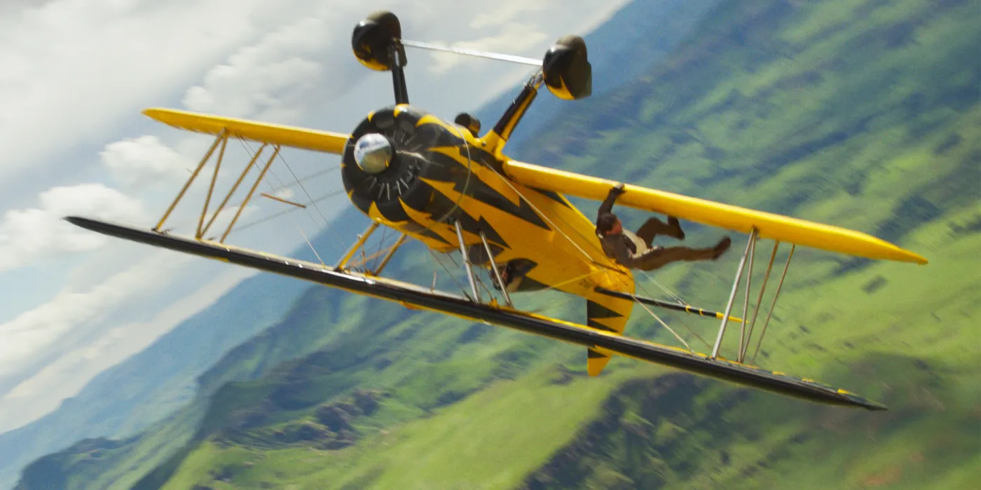 ein gelbes Flugzeug schlägt ein Looping, ein Mann hängt an einer Tragfläche