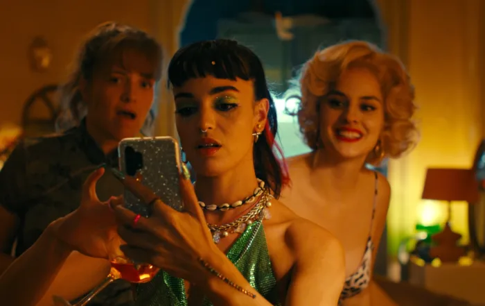 Ruby (Souheila Yacoub, Mitte) erhält eine Nachricht vom geheimnisvollen Nachbarn gegenüber. Auch Nicole (Sanda Codreanu, links) und Élise (Noémie Merlant, rechts) sind gespannt, was er schreibt.