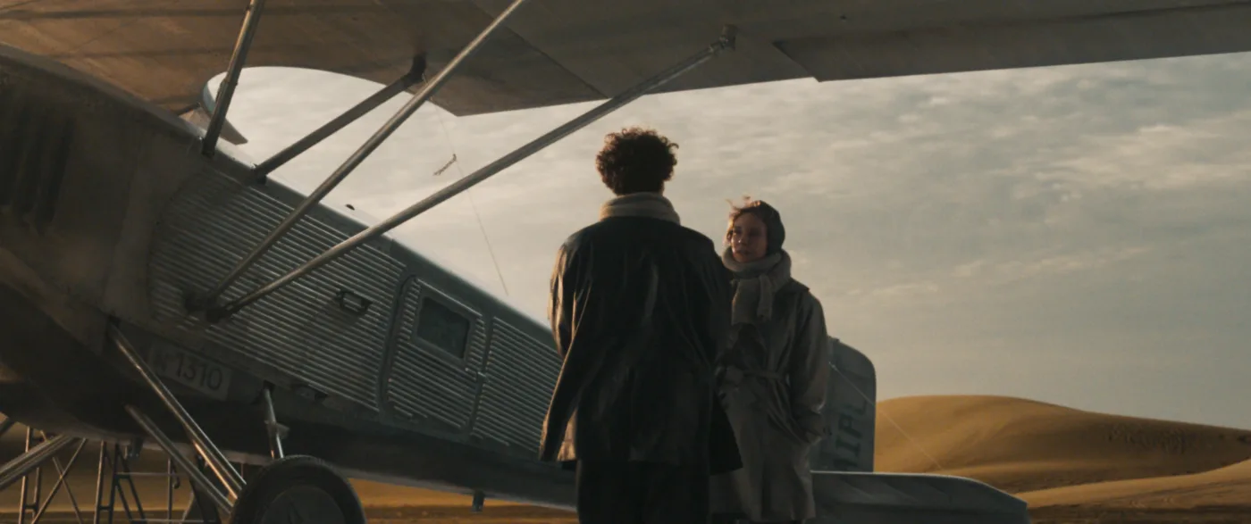 vor einem kleinen Flugzeug in einer Wüstenlandschaft stehen sich ein Mann und eine Frau gegenüber und unterhalten sich