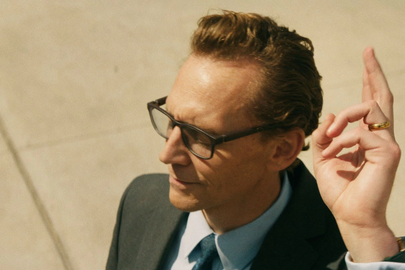 Nahaufnahme von Tom Hiddleston als Chuck, der mit geschlossenen Augen und im Anzug vor hellem Hintergrund steht und seine rechte Hand hebt
