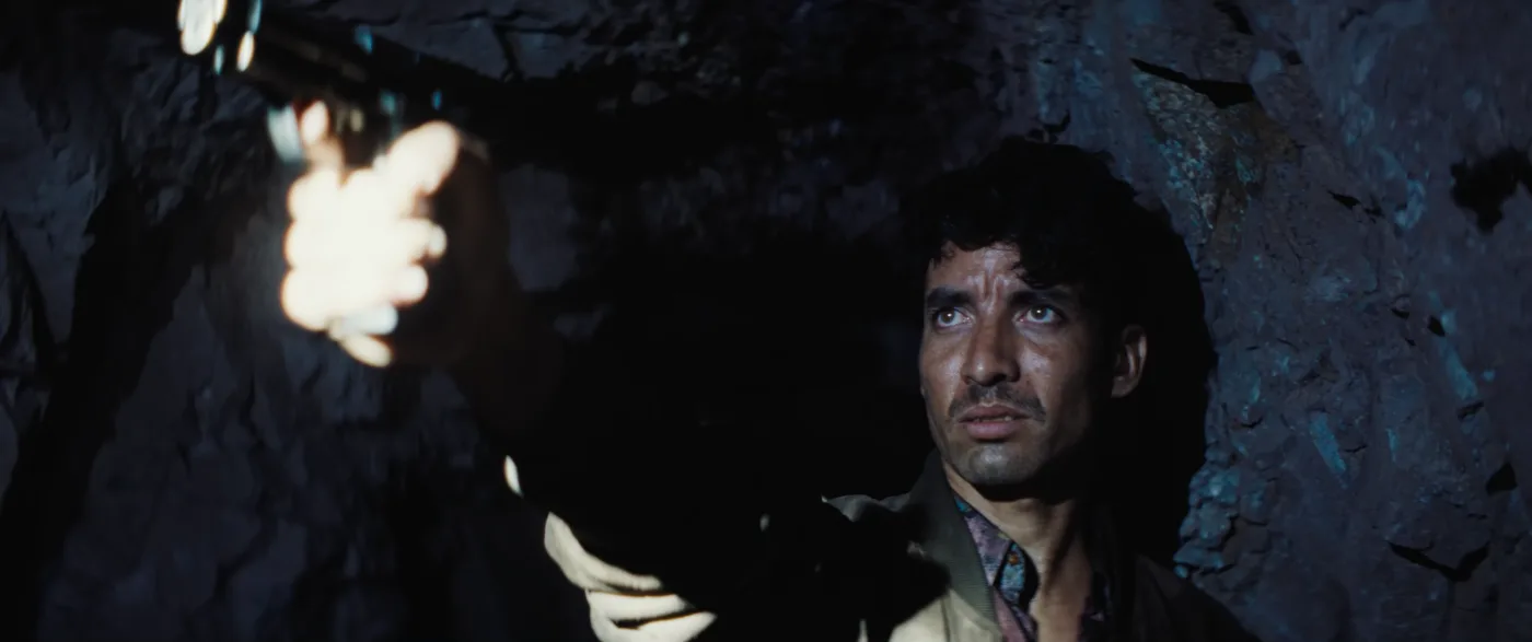 ein Mann in einer Mine, Taschenlampenlicht erhellt sein Gesicht und seine rechte ausgestreckte Hand in der er eine Waffe hält