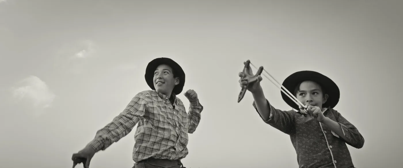 zwei Jungen mit Cowboyhüten aus Froschperspektive die mit Schleudern spielen