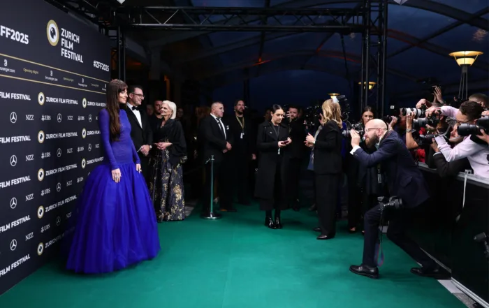 Blick auf den grünen Teppich des 21. Zurich Film Festival, wo zahlreiche Fotograf:innen und Gäste versammelt sind, während eine Schauspielerin (Dakota Johnson) in einem auffälligen blauen Kleid für Fotos posiert