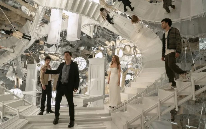 Mehrere Personen stehen und gehen auf weißen Treppen, die sich in verschiedene Richtungen winden und scheinbar in einem endlosen Muster fortsetzen. Die Umgebung besteht aus zahlreichen Spiegeln, die die Figuren und Treppen vielfach reflektieren. Eine Frau trägt ein langes, weißes Kleid. [erstellt mit KI]