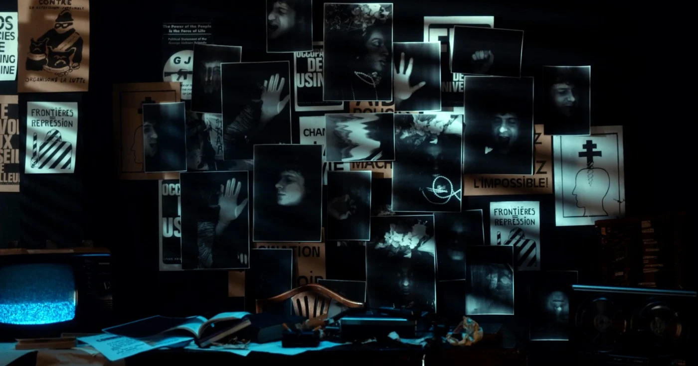 Mehrere Fotografien mit Händen und Gesichtern sind auf einer dunklen Wand angeordnet. Die Bilder sind teilweise überlappend und werden von Lichtstrahlen hervorgehoben. Im Vordergrund liegen ein aufgeschlagenes Buch, ein Telefonhörer und weitere Gegenstände auf einem Tisch. Links unten steht ein alter Röhrenfernseher mit blauem Bildschirm. Im Hintergrund sind Plakate mit klar lesbaren Buchstaben und Symbolen zu erkennen. [erstellt mit KI]