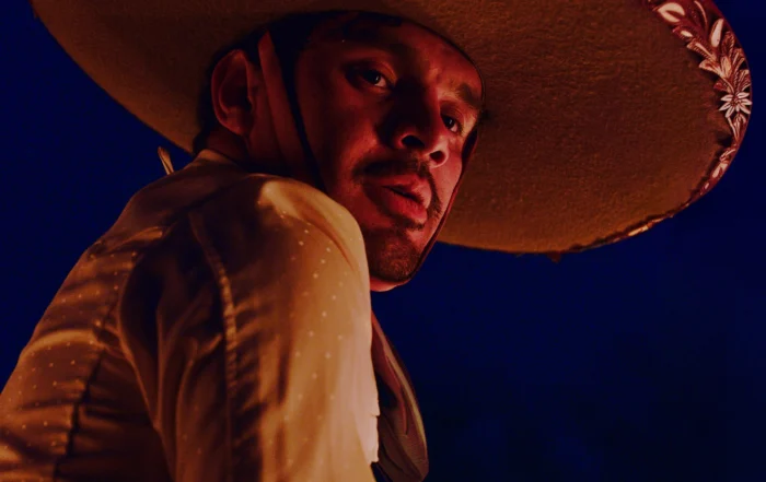 Ein Mensch trägt einen großen, runden Hut mit dekorativem Muster am Rand. Das Hemd ist hell und mit feinen Punkten versehen. Der Hintergrund ist dunkelblau und erzeugt einen starken Kontrast zu der Kleidung und dem Hut. [erstellt mit KI]