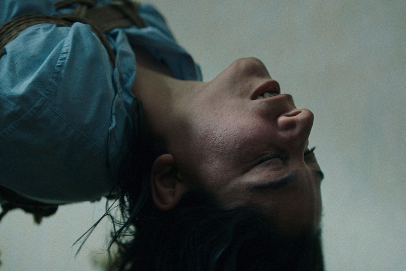 Szenenbild von Lust: Nahaufnahme einer Frau im blauen Oberteil, die mit geschlossenen Augen in Seilen hängt