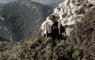 Szenenbild aus Les Misérables - Die Geschichte von Jean Valjean: In einer bewaldeten Gebirgslandschaft steht ein Mann mit Bart und Wanderstock.
