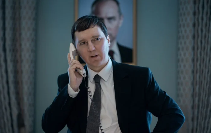 Szenenbild aus Der Magier im Kreml: Ein Mann im Anzug und Schlips am Telefon vor einem Porträt Putins.