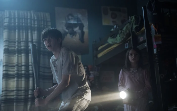 Szenenbild aus Lee Cronin's The Mummy: In einem dunklen Zimmer stehen zwei Kinder im Schlafanzug. Rechts steht ein Mädchen mit Taschenlampe, links ein älterer Junge mit einem Schläger in den Händen.