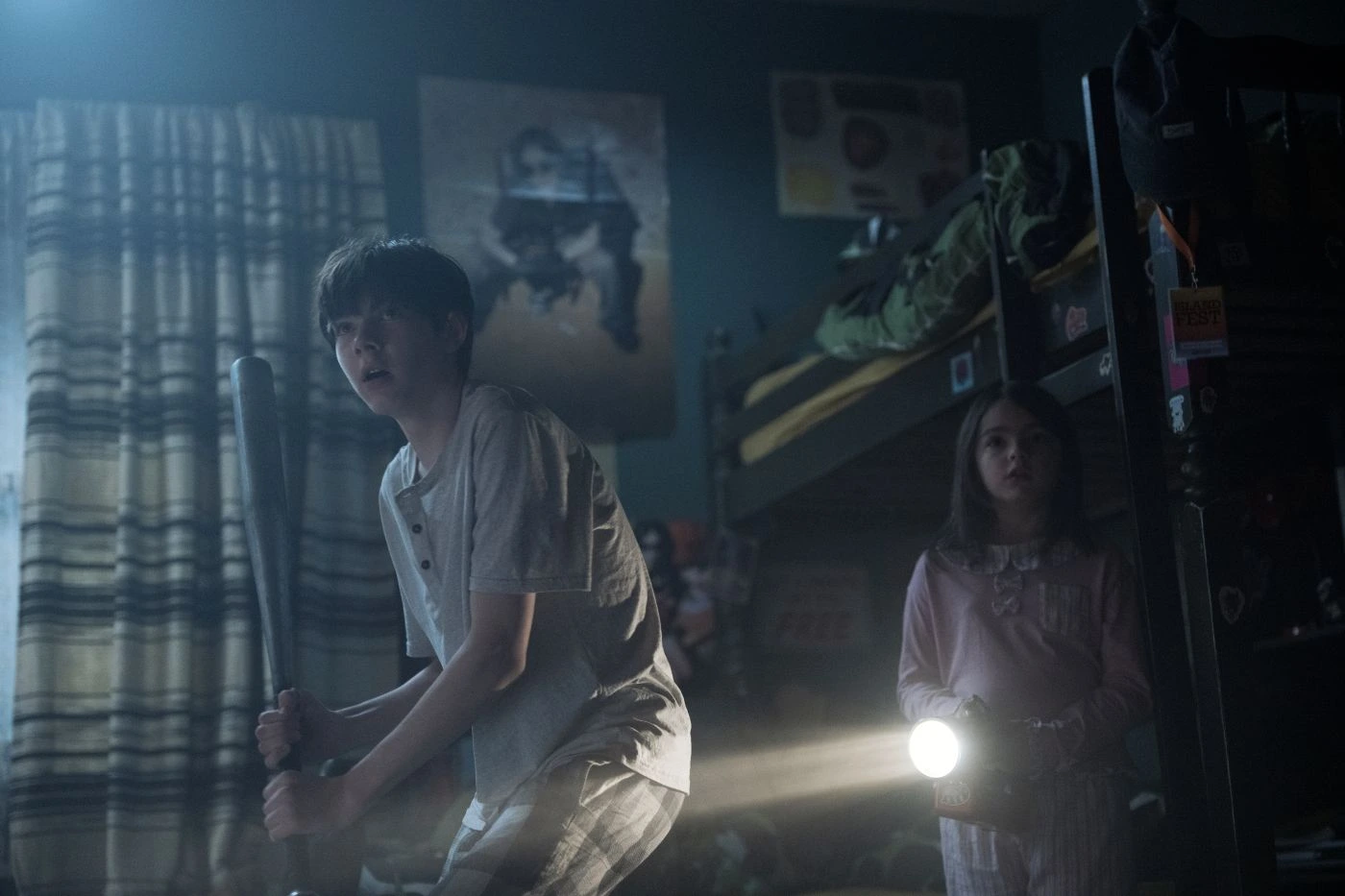 Szenenbild aus Lee Cronin's The Mummy: In einem dunklen Zimmer stehen zwei Kinder im Schlafanzug. Rechts steht ein Mädchen mit Taschenlampe, links ein älterer Junge mit einem Schläger in den Händen.