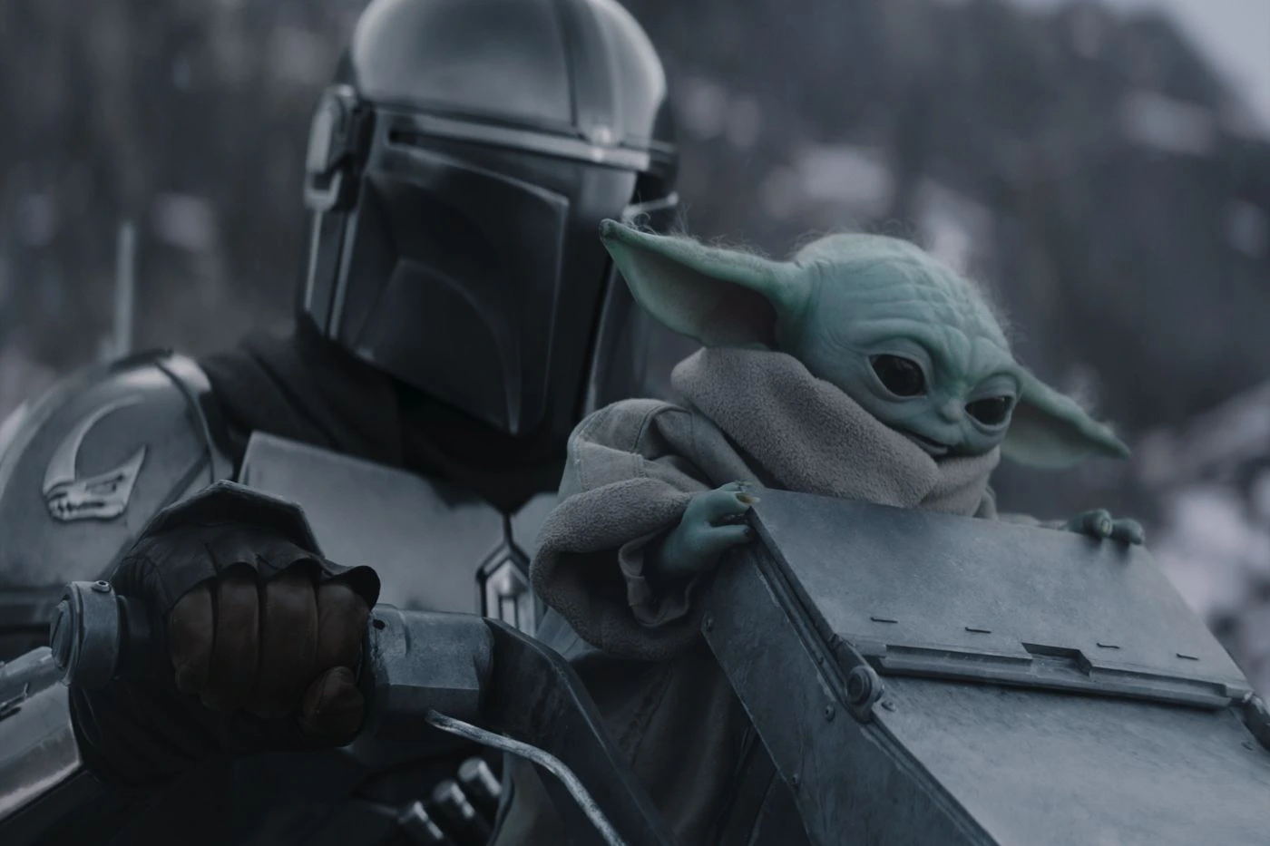 Szenenbild aus The Mandalorian and Grogu: Eine gepanzerte Figur mit glänzendem Helm hält ein metallisches Objekt, während eine kleine, grünhäutige Kreatur mit großen Ohren und einem beigefarbenen Umhang daneben sitzt. [erstellt mit KI]